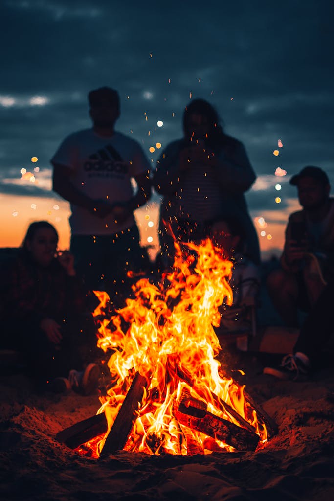 A group of friends enjoying a bonfire on the beach at twilight, creating a warm and inviting atmosphere.